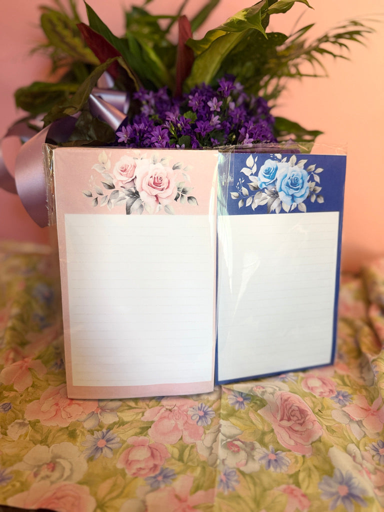 Two floral rose notepads in blush pink and navy blue with watercolor rose designs