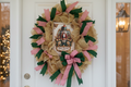 Nutcracker Merry Christmas gold mesh wreath with pink and green ribbons hanging on a white front door